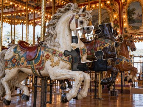 Three painted carousel horses among brass poles, warm bulbs and ornate vintage woodwork.