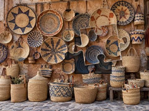 Wall of handmade woven baskets and trays with natural straw, indigo and rust-colored patterns.